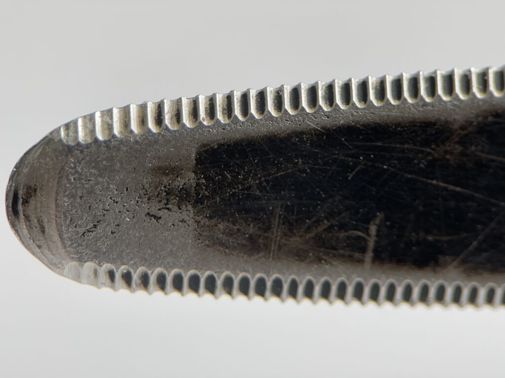 Extreme close-up of CANARY cardboard cutter tip showing fine serrated edge and wear on black steel blade