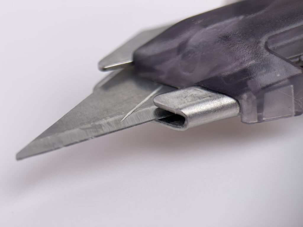 Macro photograph of the tip of the DAT-X box cutter blade, showing the edge sharpness and blade holder construction.