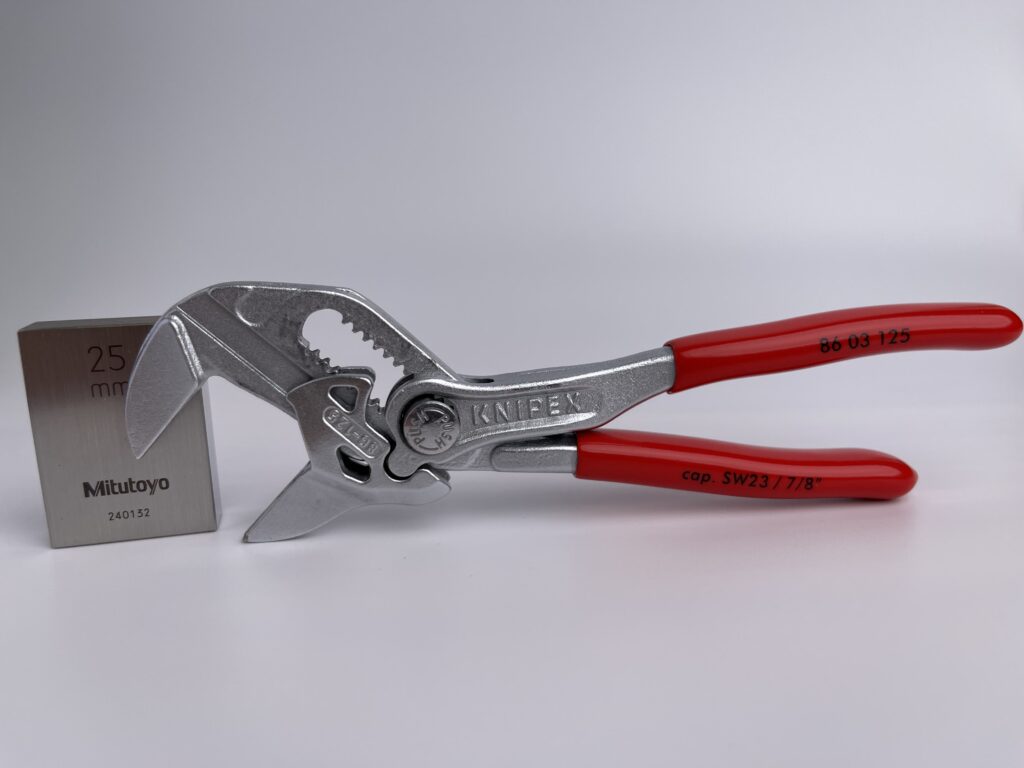 Side profile of the KNIPEX 86 03 125 mini pliers wrench with red plastic grips, positioned next to a 25mm Mitutoyo gauge block for scale reference.