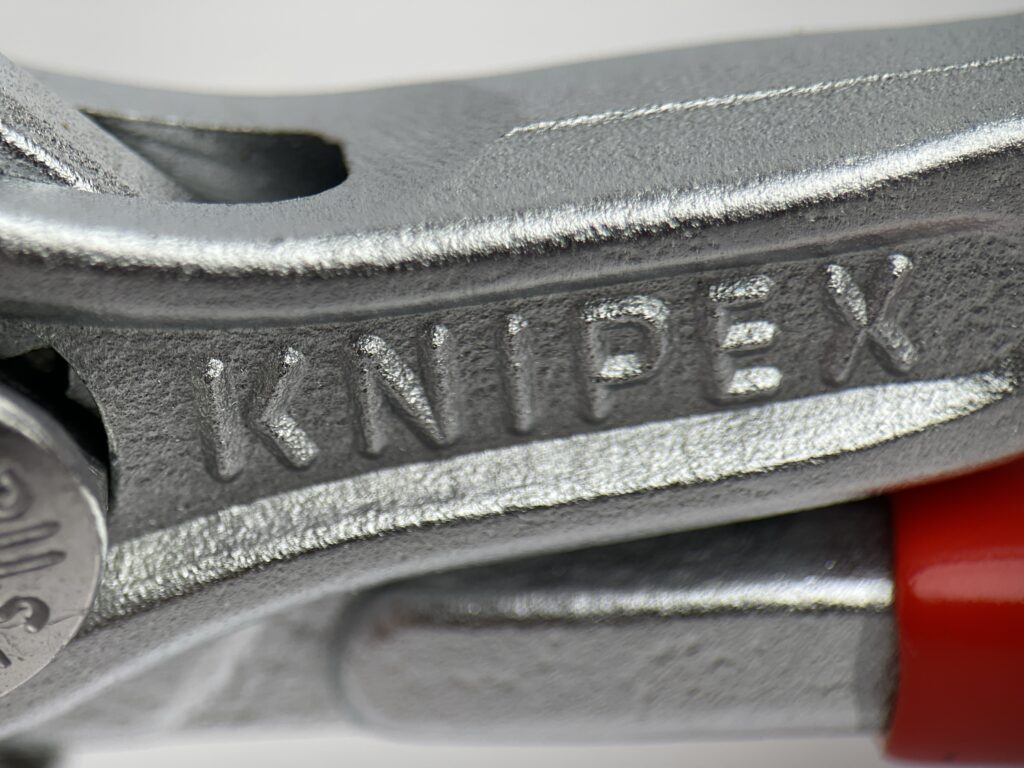 Detailed macro shot of the KNIPEX branding cast into the body of the 86 03 125 mini pliers wrench, highlighting the tool's forged finish and German manufacturing quality.