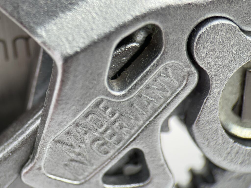 Extreme macro close-up of the "Made in Germany" text embossed on the forged steel body of the KNIPEX 86 03 125 mini pliers wrench, showcasing precision craftsmanship.